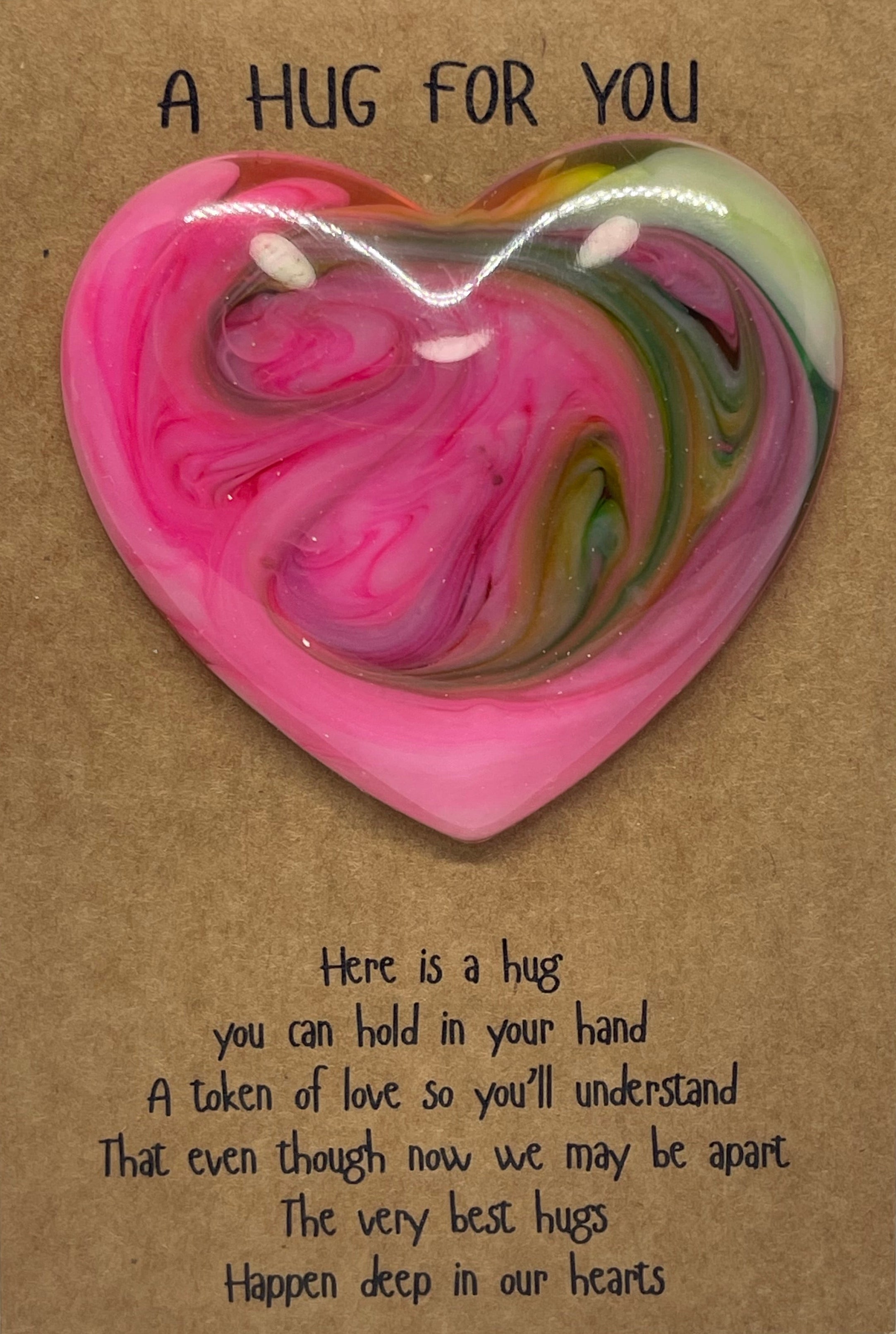 Heart-shaped pink and green swirled hug pillow on a brown card with text.