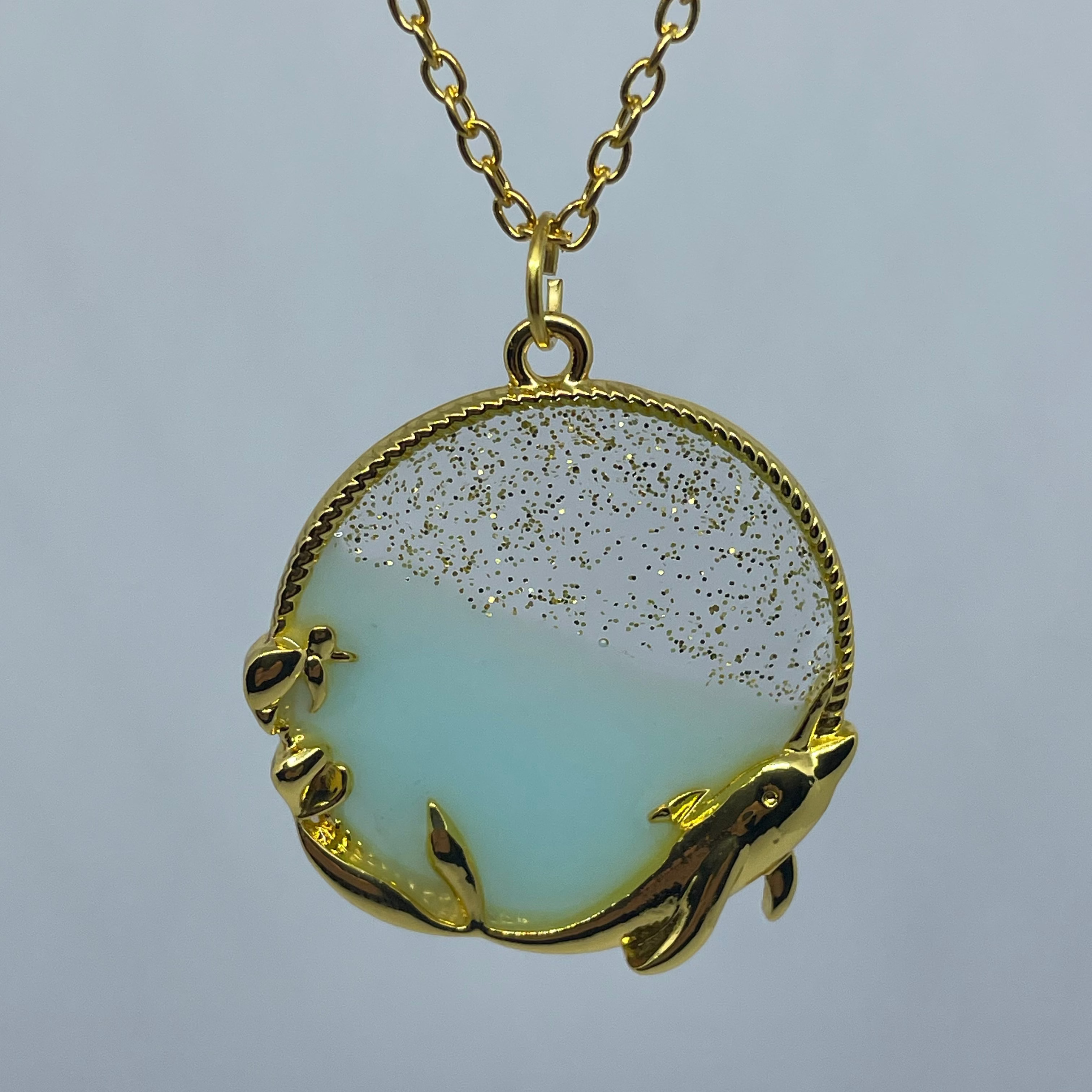 Gold necklace with a pendant featuring dolphins on a light gray background