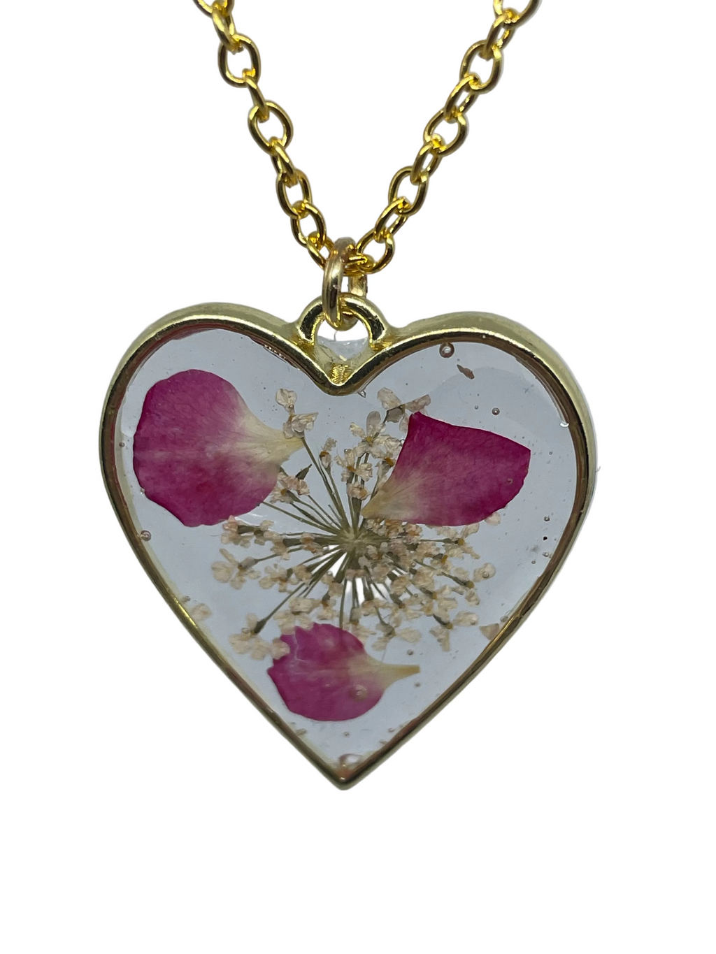 Heart-shaped pendant with pressed flowers on a gold chain against a light gray background